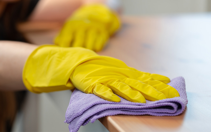 Professional cleaner in yellow gloves deep cleaning a wooden surface.