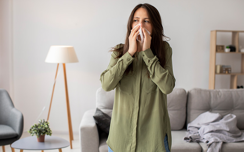 Woman sneezing due to dust allergies in a home.