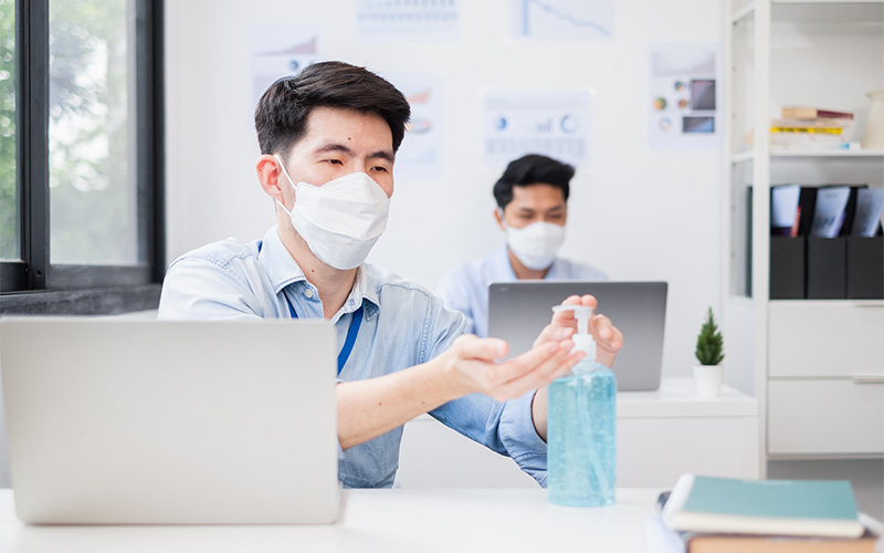 Masked employee using hand sanitizer to stop spreading sickness.