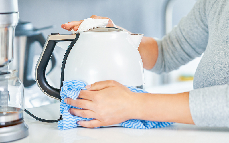 Wiping the exterior of a white electric kettle during cleaning
